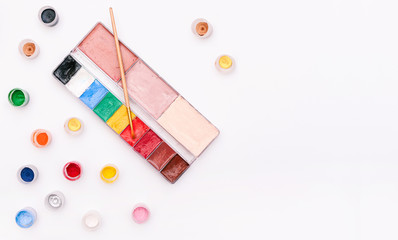 Palette with paints and brush isolated on a white background. Colored small jars of paint. Set of artist for make-up and drawing. Top view, copy space.
