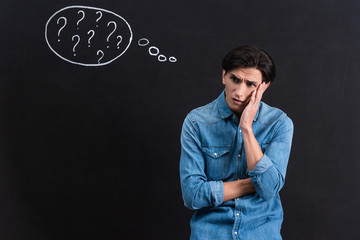 worried young man with question marks in thought bubble on blackboard