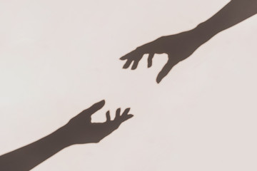 Grey shadows of hands reaching each other on the wall. Abstract blurred effect.