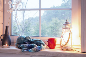 Festive lantern, red mug and heart on a wooden window sill in winter indoors.