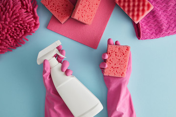 cropped view of housekeeper in pink rubber gloves holding sponge and spray bottle on blue with rags