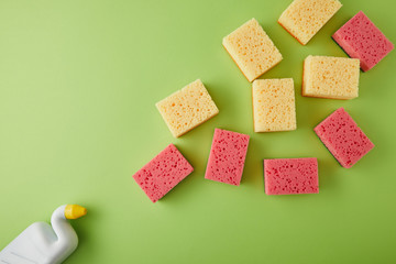 top view of pink and yellow sponges and bottle with toilet cleaner on green