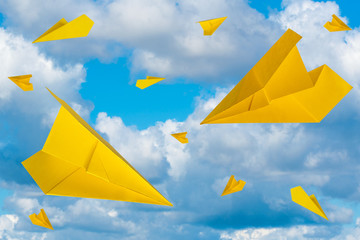 Yellow paper planes flying in a cloudy sky