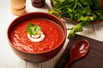 Tomato soup in a brown clay bowl with milk cream on a white wooden background