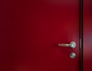 Semi-abstract close-up of part of a red door with metal handle and lock in natural light