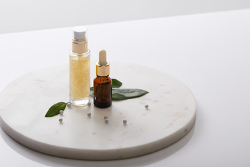 Bottles of cosmetic oil with leaves and decorative beads on round stand isolated on grey