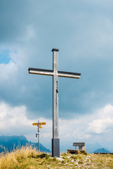 Large wooden cross, mountain trail signs and wooden bench on top of a mountain. Alpine peak, Monte Boglia, Lugano, Switzerland.