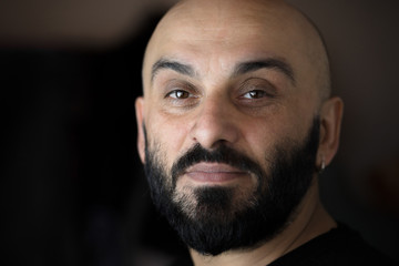 Close-up portrait of a bearded bald man with earring with black, dark background