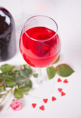 Glass of red grape wine with bottle and roses on the background. Romantic dinner concept.