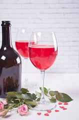 Two glasses with red grape wine with bottle and roses on the background. Romantic dinner concept.