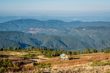 Rila Mountain in Bulgaria at sunny autumn day, a small wooden mountain shelter, alternating green mountain ranges in the background.