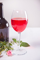Glass of red grape wine with bottle and roses on the background. Romantic dinner concept.