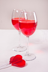 Glasses of red grape wine with red candies heart shape on the white background