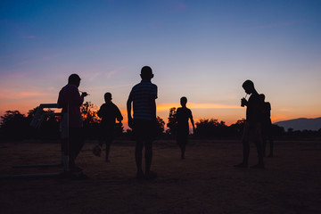 Fototapeta na wymiar Silhouette action sport outdoors of a group of kids having fun playing soccer football for exercise in community rural area under the twilight sunset sky.