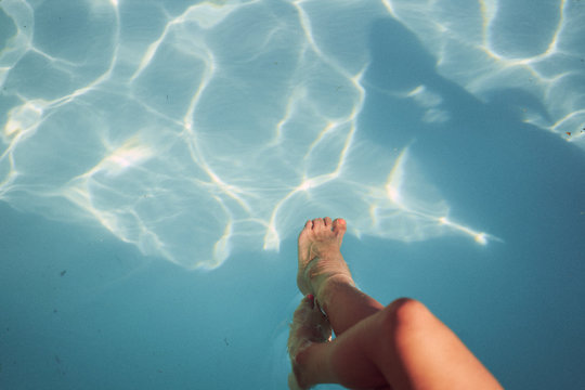 Women dangling feet into pool