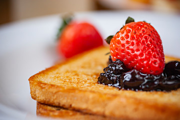 Table top close up of bread toast with the toppings of cranberry jam and Strawberry in white plate on wooden dining table.