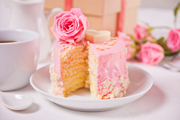 Mini small cake with pink glaze, beautiful roses, cup of coffee, gift box on the white table.