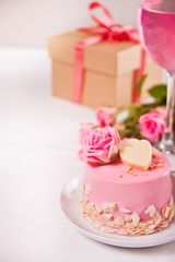 Obraz na płótnie Canvas Mini small cake with pink glaze, beautiful roses, cup of coffee, gift box on the white table.