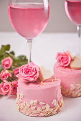 Two mini cakes, glasses with pink grape wine and rose flowers on a white table. Romantic dinner concept