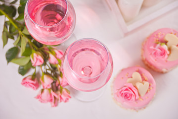 Obraz na płótnie Canvas Two glasses with pink grape wine with rose flowers and mini cakes. Romantic dinner concept.