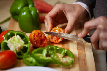 Close-up of hands chopping fresh green red tomato on wooden chopping board in domestic kitchen.