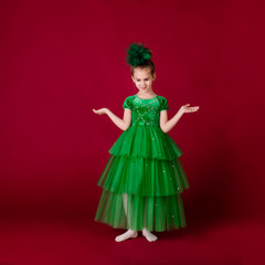 Beautiful little girl princess dancing in luxury green dress isolated on red background. Carnival party with costumes