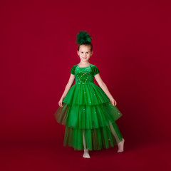 Beautiful little girl princess dancing in luxury green dress isolated on red background. Carnival party with costumes
