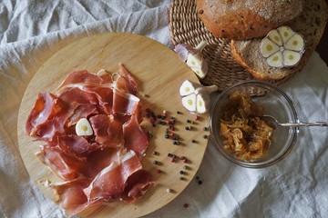  A snack of prosciutto, cereal ciabatta and homemade onion marmalade, served with fresh garlic and colorful pepper