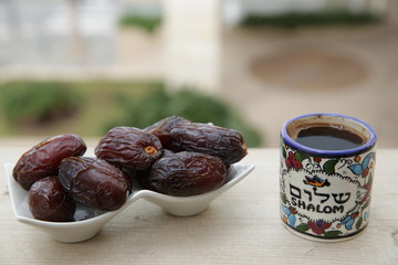 Sweet dates and black coffee in a cup with the inscription shalom in a soft blur of the street background. Breakfast in Israel.