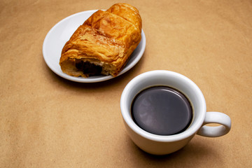 Coffee in a white cup on a saucer bitten croissant on a beige background