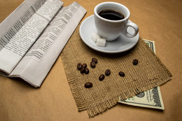 White cup with coffee on a napkin, dollars, newspaper, on a beige background