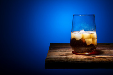 Glass glass with ice cubes and carbonated drink standing on a wooden table on a gradient dark background