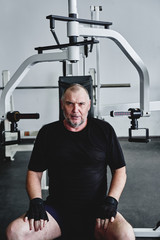 Fototapeta na wymiar Adult gray-haired man trains on fitness equipment in the gym, pumps legs and arms muscles, loses weight. Concept of healthy lifestyle in old age