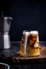 cold late coffee drink with ice. Ice coffee on a wood table with cream being poured into it showing the texture