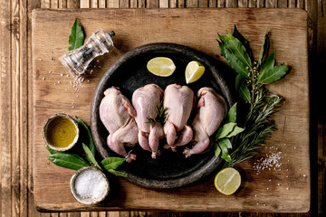 Raw uncooked quails ready for marinat in clay tray with lime, salt, pepper and greens over wooden...