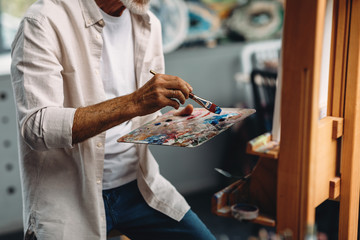 Male hand holding paintbrush and mixing oil paints on colorful messy palette © Artem Varnitsin