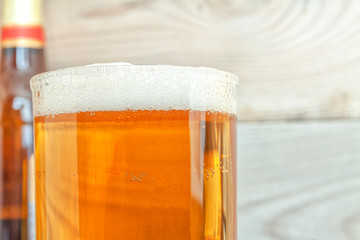 A mug with beer and foam against the background of a bottle and a wooden background.