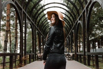 Happy beautiful girl having fun walking in wooden tunnel in park. Portrait of young smiling woman in hat. Joint vacation concept. Lovely girl posing in in the old street