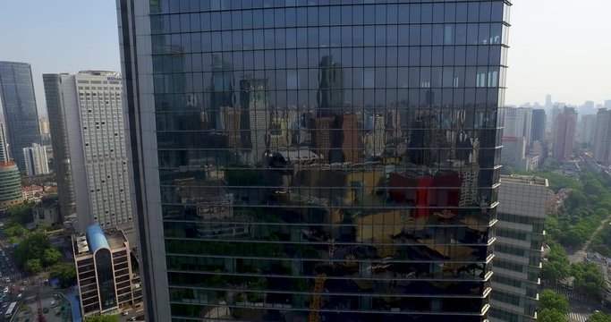 Moving up reflective skyscraper aerial shot.  Giant glass office building in downtown reflecting cityscape during daytime. Rising up on office windows drone shot.