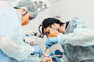 Two male dentists perform an operation on a patient. Surgery in dentistry. Professional uniform and equipment of a dentist. Healthcare Equipping a doctor’s workplace. Dentistry