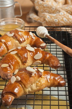 Top view, close distance of three honey, almond crescents, cooling on a wire screen with a honey aplicator and a glass bowl of honey