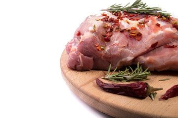 Pork tenderloin in one piece, rosemary, chili pepper, spices on a round wooden cutting Board on a white isolated background
