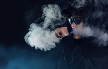 vape man. portrait of a handsome guy in a black cap and glasses vaping and exhaling a cloud of...
