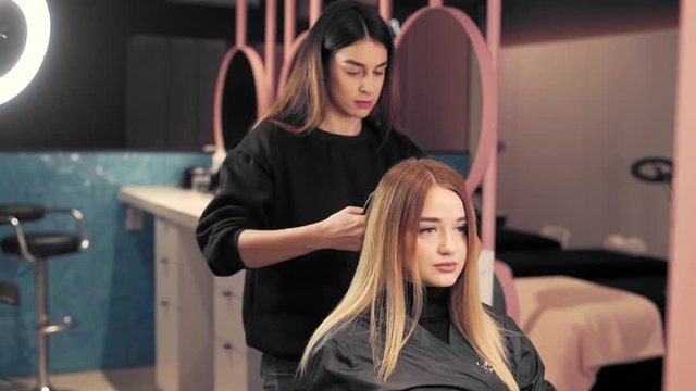 Hairstylist combs the hair of a beautiful girl in a beauty salon