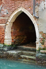 Entrance in an old brick wall near water in Venice
