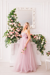 Beautiful blonde girl in a long soft purple dress on a background of flowers posing. A young woman in the image of a Princess.Lush lilac dress. The concept of perfumes, fashion and beauty