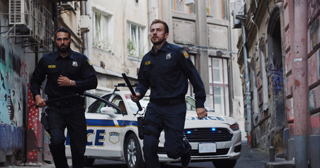 Police patrol car arrives at crime scene. Bottom view professional cops with handguns running in...