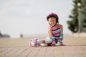 little blonde girl in colorful clothes rides on roller skates in the summer in the Park