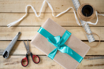 handmade gift box tie a green bow, a tool for its manufacture on a wooden background, top view, copy space