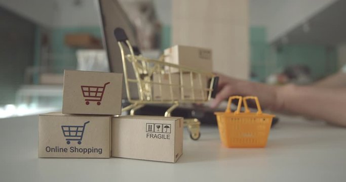 Online shopping / ecommerce and delivery service concept : Paper cartons with a shopping cart or trolley logo, user uses a laptop, depicts customers order things from retailer sites via the internet.